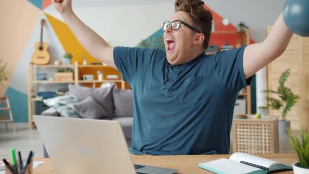 Playful guy receiving good news online using laptop celebrating success at home — 비디오