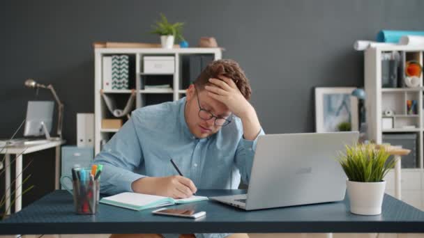 Yorgun genç adam iş yerinde bilgisayarla yazıp çalışıyor. — Stok video