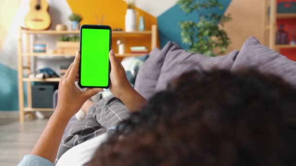 Rückansicht einer afroamerikanischen Frau, die sich Inhalte des grünen Smartphone-Bildschirms ansieht — Stockvideo