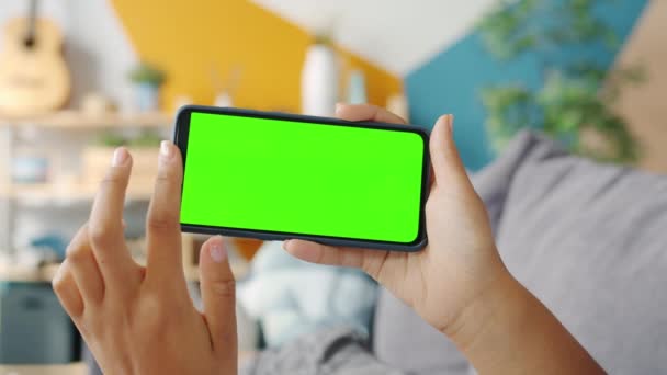 Повільний рух рук дівчат, які торкаються зеленого вертикального екрану смартфона в приміщенні — стокове відео