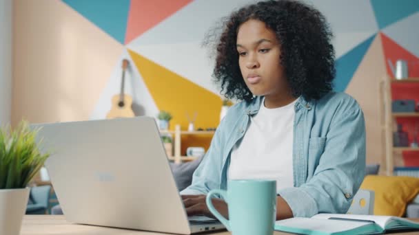 Câmera lenta de mulher afro-americana bonito usando laptop em casa escrevendo em notebook — Vídeo de Stock