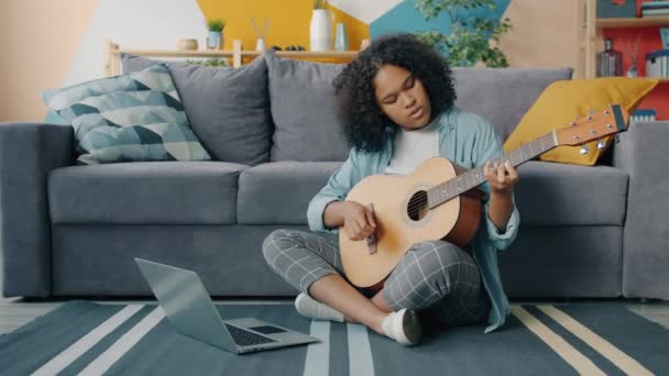 Blandad ras ung kvinna lär sig att spela gitarr med laptop hemma — Stockvideo