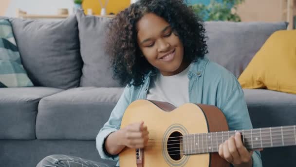 Feliz jovem mulher de raça mista tocando guitarra e usando laptop no apartamento — Vídeo de Stock