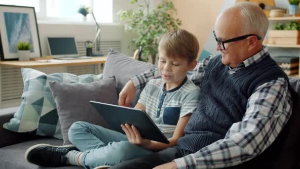 Glücklicher Opa im Gespräch mit fröhlichem Kind mit Tablet entspannen zusammen zu Hause — Stockvideo