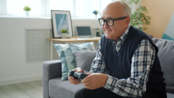 Портрет літнього чоловіка, який грає у відеоігри в квартирі, насолоджуючись перемогою — стокове відео