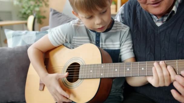 Elderly man teaching grandson to play the guitar in apartment bonding — 비디오