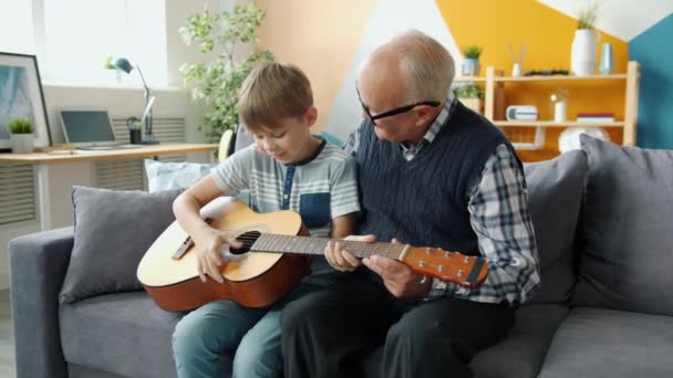 Αργή κίνηση χαρούμενων ανθρώπων εγγονός και παππούς παίζει κιθάρα στο σπίτι — Αρχείο Βίντεο