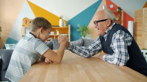 Happy child enjoying arm wrestling with loving grandfather in apartment — ストック動画