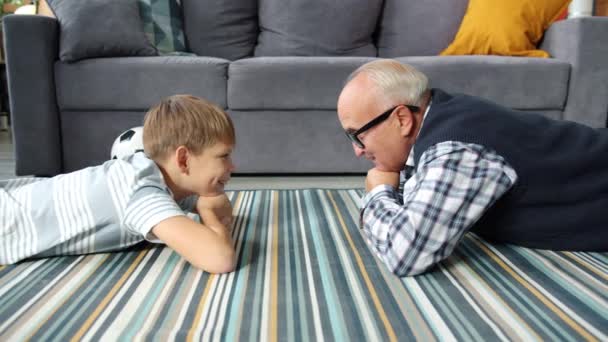 Cámara lenta del abuelo y el nieto hablando relajándose en el suelo en casa — Vídeos de Stock