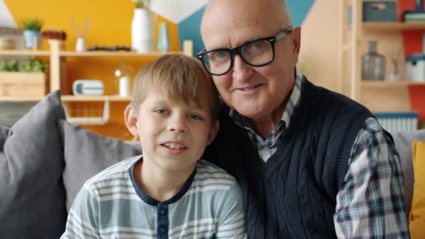 Портрет діда і онука, який дивиться на камеру, посміхаючись вдома — стокове відео