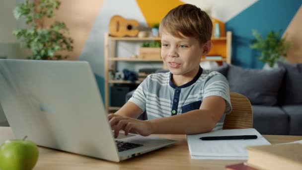 Радостный ребенок делает домашнее задание, используя ноутбук, а затем делает заметки в блокноте — стоковое видео
