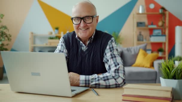 Портрет повільного руху усміхненого старшого чоловіка, який дивиться на камеру, сидячи за комп'ютером — стокове відео