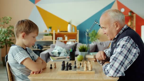 Portret van opa en kleinzoon die schaak spelen bewegende schaaksters aan boord — Stockvideo