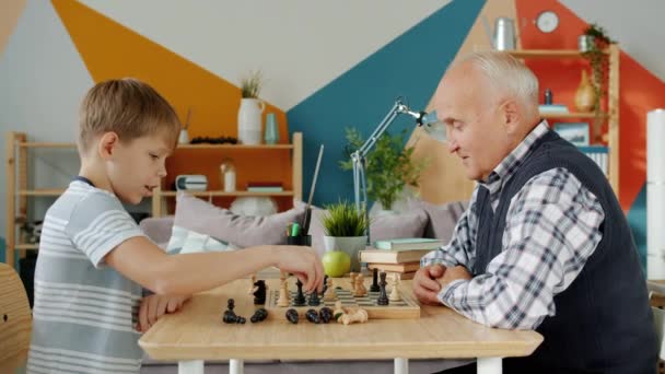 Χαρούμενο παιδί που παίζει σκάκι με τον παππού να κερδίζει γελώντας. — Αρχείο Βίντεο