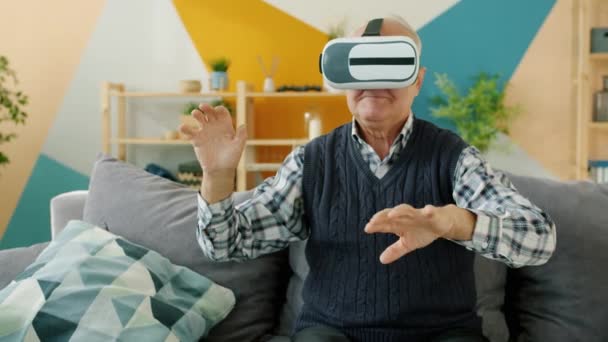 Senior man using virtual reality glasses and gesturing sitting on sofa in apartment — 비디오