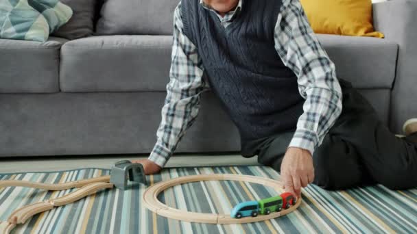 Stařec v důchodu hrát s dřevěnými autíčky sedí na podlaze v bytě — Stock video