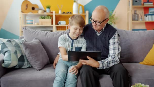 Langzame beweging van opa en kleinzoon met behulp van tablet thuis lachen praten — Stockvideo