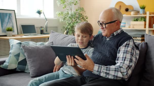 Ηλικιωμένος άνδρας και ευτυχισμένο αγόρι χρησιμοποιώντας tablet μιλώντας απολαμβάνοντας ελεύθερο χρόνο και gadget — Αρχείο Βίντεο