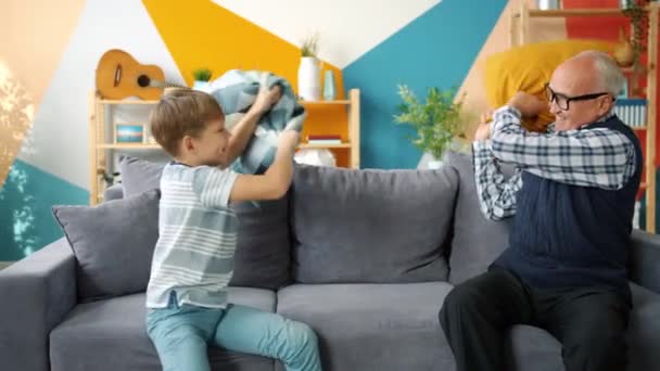 Großvater spielt mit fröhlichem Kind, das Kissen bekämpft und Spaß in Wohnung hat — Stockvideo