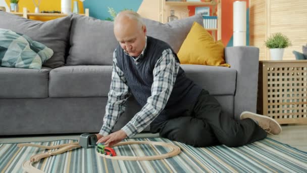 Starší muž dědeček hraje pohyblivé hračky auta sedí na podlaze doma — Stock video