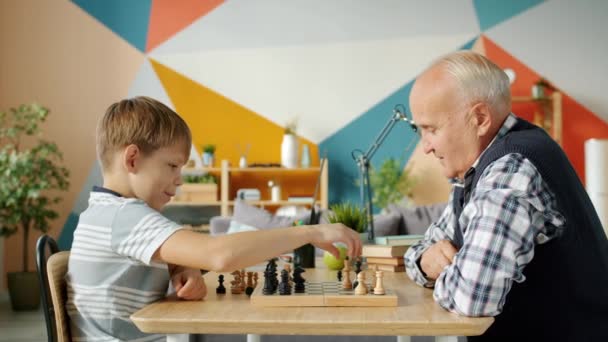 Glada människor gammal man och barn spelar schack i lägenheten pratar leende — Stockvideo