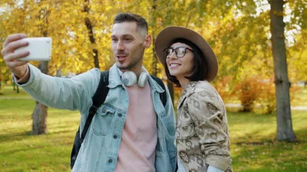 Piękne dziewczyna i facet biorąc selfie z smartfon aparat na zewnątrz w park — Wideo stockowe