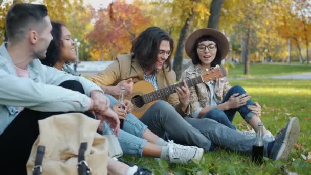 Lassú mozgás vidám fiúk és lányok szórakozás gitározni énekel a parkban — Stock videók