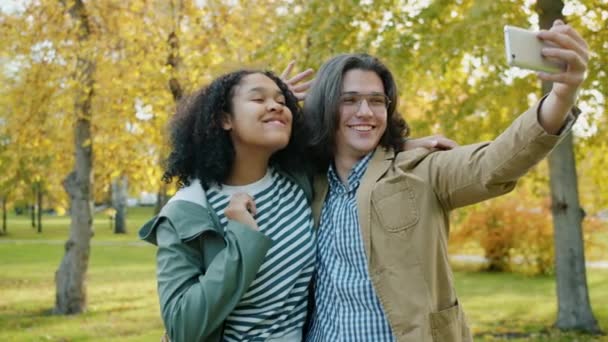 Kız ve erkeğin parkta selfie çekmesi, sarılmaları, jestlerle eğlenmeleri. — Stok video