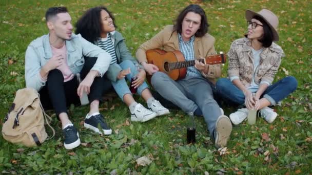 Hög vinkel syn på manliga och kvinnliga vänner spelar gitarr sång i parken — Stockvideo