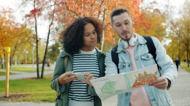 Mieszane wyścigi para turystów patrząc na mapę rozmowy podróżujących w parku miejskim — Wideo stockowe