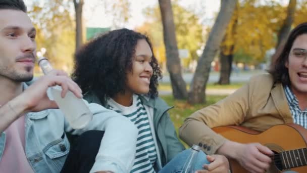 Retrato de jóvenes felices cantando la guitarra en el parque de la ciudad en otoño — Vídeo de stock