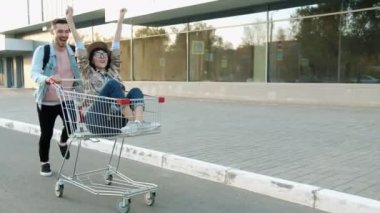 Mutlu bir adam alışveriş arabasını iterken heyecanlı bir kız şehirde oturmuş eğleniyor.