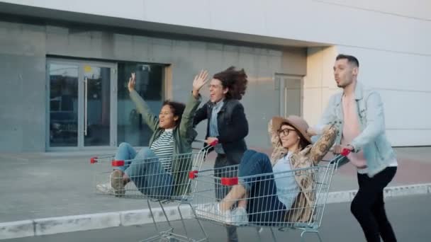 Grupo de amigos estudiantes divirtiéndose en la ciudad montando carritos de compras riendo — Vídeo de stock