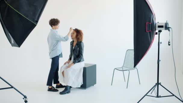 Maquillaje artista trabajando en la colocación de cosméticos en modelo de mujer joven en el estudio — Vídeos de Stock