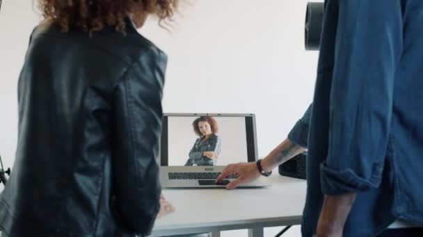 Rückansicht von Mann und Frau beim Betrachten von Fotos auf Laptop-Bildschirm im Fotostudio — Stockvideo