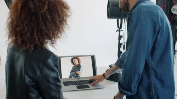 Fotografo che mostra le foto al modello di razza mista utilizzando il computer portatile in studio — Video Stock
