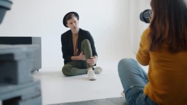 Moda kıyafetleri içinde şık bir adam fotoğraf stüdyosunda kadın fotoğrafçıya poz veriyor.