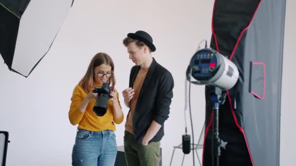 Cámara lenta del hombre y la mujer viendo imágenes en la cámara hablando en el estudio de fotos — Vídeos de Stock