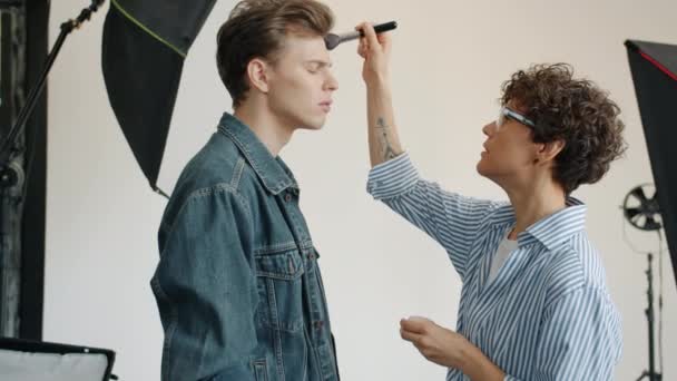 Maquillaje artista poner cosméticos en los modelos masculinos cara en el estudio de fotos antes de la sesión de fotos — Vídeos de Stock