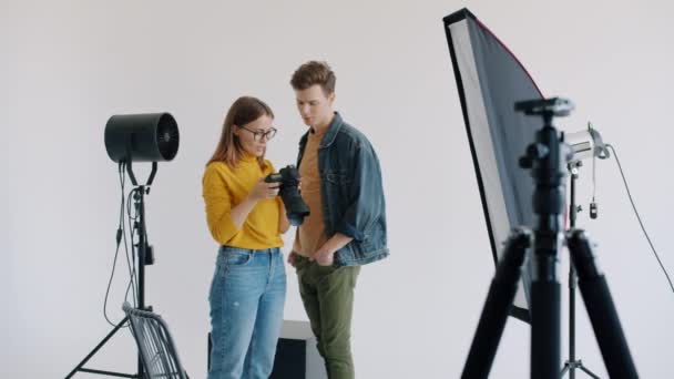 Дівчина і хлопець модель дивитися фотографії в студії обговорюють фотосесію — стокове відео
