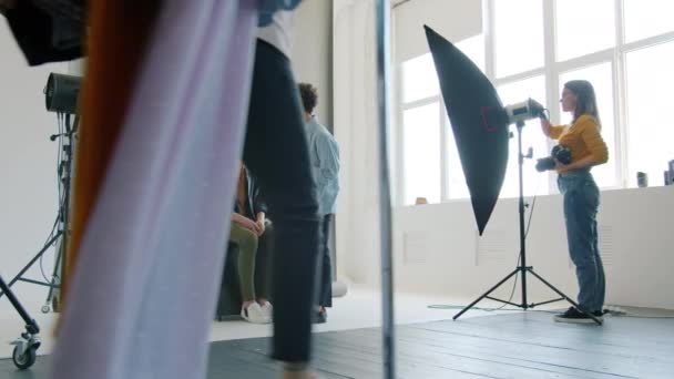 Maquiagem artista trabalhando com modelo enquanto estilista cabide em movimento com roupas em stydio — Vídeo de Stock