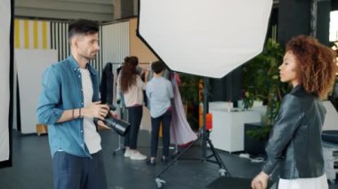Modern stüdyoda erkek fotoğrafçının kız mankenleri vurması ağır çekimdir.