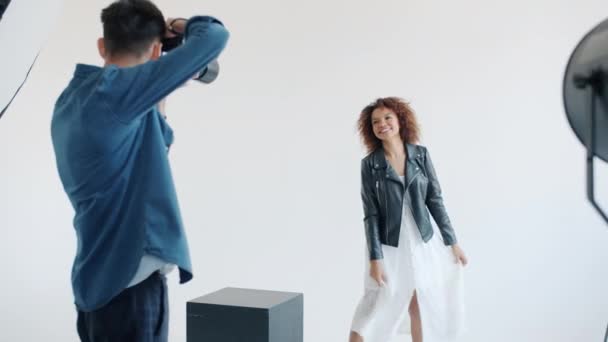 Modelo sonriente posando sobre fondo blanco para fotógrafo con cámara — Vídeos de Stock