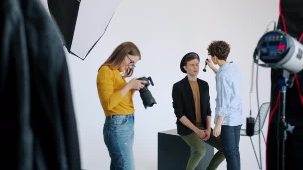 Movimento lento de maquilhadora trabalhando com modelo masculino no estúdio de fotografia — Vídeo de Stock