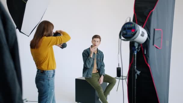 Jóképű férfi pózol a stúdióban, aztán női fotóssal beszél. — Stock videók