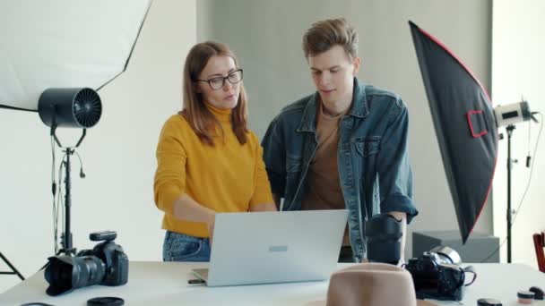 Vidám fiatalok férfi és nő néz képeket a stúdióban a laptop — Stock videók