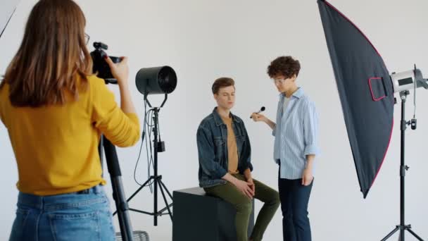 Modelo de cara atraente trabalhando com visagiste, em seguida, posando para fotógrafo em estúdio — Vídeo de Stock