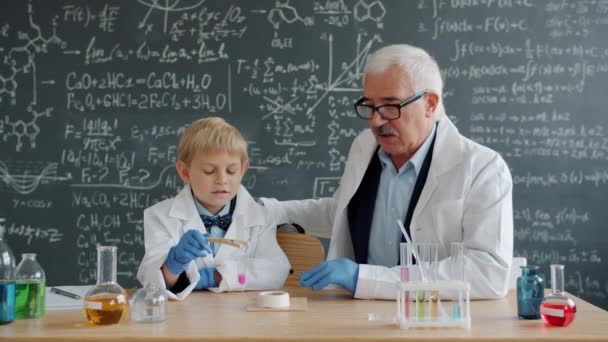 Little boy condusting chemical test at school while teacher helping explaining — Stockvideo