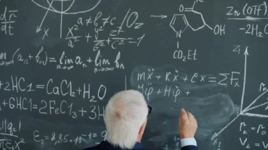 Yaşlı adamın tahtaya hesaplamalar ve formüller yazarken yavaş çekim görüntüsü