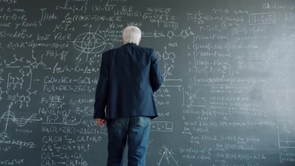 Homme âgé intelligent marchant au tableau avec des formules dans la salle de classe universitaire — Video